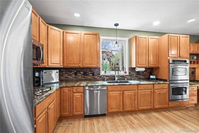 5049 Heatherglen Dr, Highlands Ranch, CO 80130 - kitchen with stainless steel appliances, a sink, light wood-style floors, tasteful backsplash, and dark stone countertops