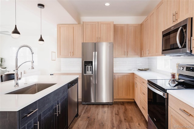 kitchen with appliances with stainless steel finishes, light brown cabinets, hanging light fixtures, and sink