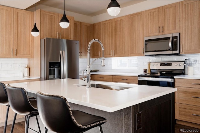 kitchen with backsplash, a kitchen island with sink, sink, decorative light fixtures, and stainless steel appliances