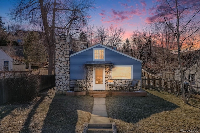 exterior space with stone siding, a chimney, a front yard, and fence