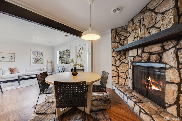 dining room featuring wood finished floors, a fireplace, visible vents, and ornamental molding