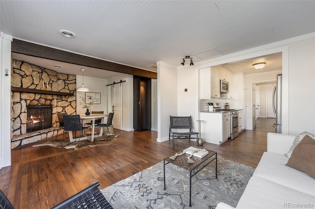 living room featuring visible vents, crown molding, a barn door, a stone fireplace, and dark wood-style floors