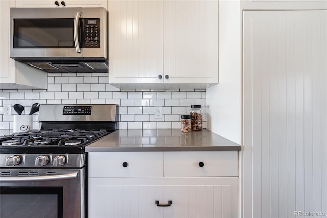 kitchen featuring stainless steel appliances, tasteful backsplash, dark countertops, and white cabinets