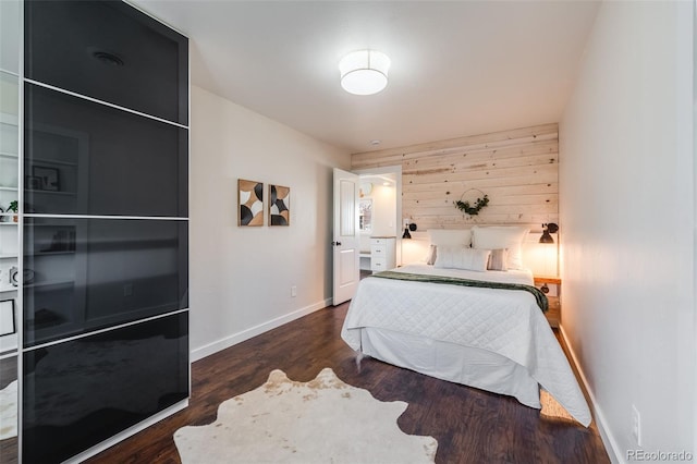 bedroom featuring an accent wall, wooden walls, wood finished floors, and baseboards