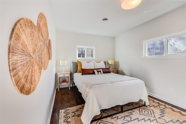 bedroom featuring baseboards, multiple windows, visible vents, and wood finished floors