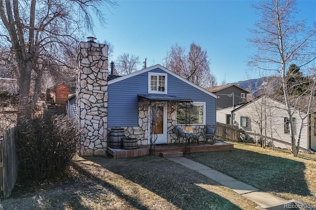 view of front of home featuring a front lawn, fence, a wooden deck, a chimney, and stone siding