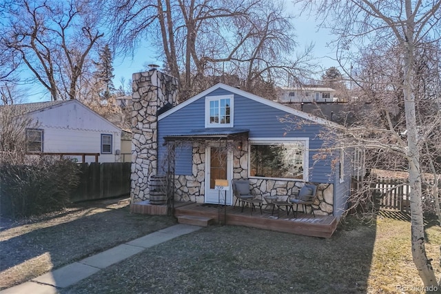 bungalow featuring stone siding, a chimney, and fence