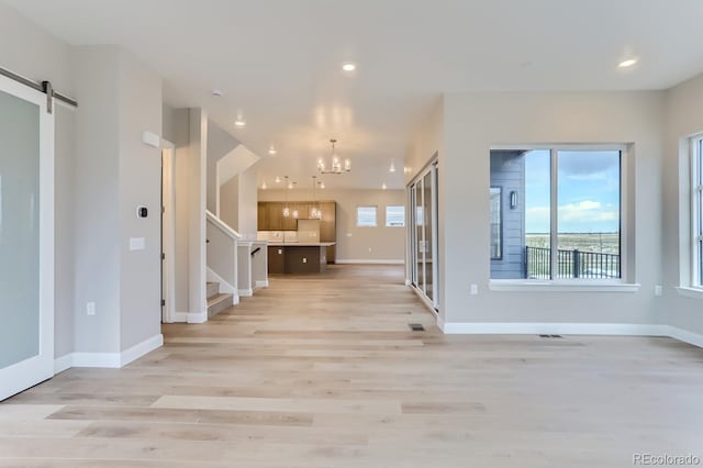 interior space with a barn door, an inviting chandelier, and light wood-type flooring