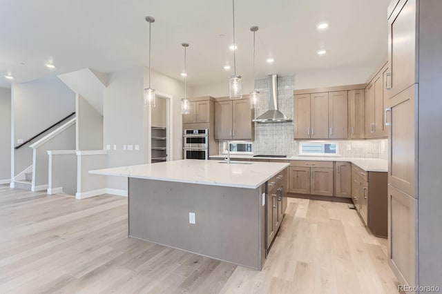 kitchen featuring pendant lighting, wall chimney exhaust hood, a spacious island, light stone countertops, and stainless steel double oven