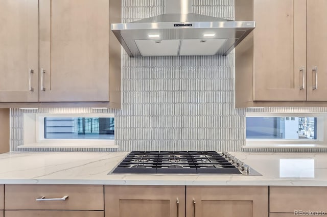 kitchen with light stone counters, stainless steel gas cooktop, tasteful backsplash, and wall chimney range hood