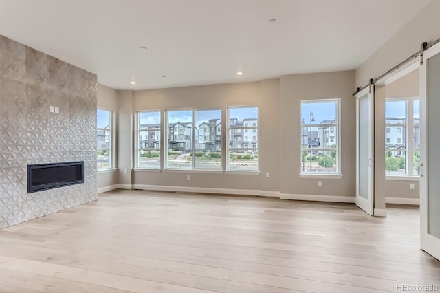 unfurnished living room featuring a barn door, a fireplace, and light hardwood / wood-style floors