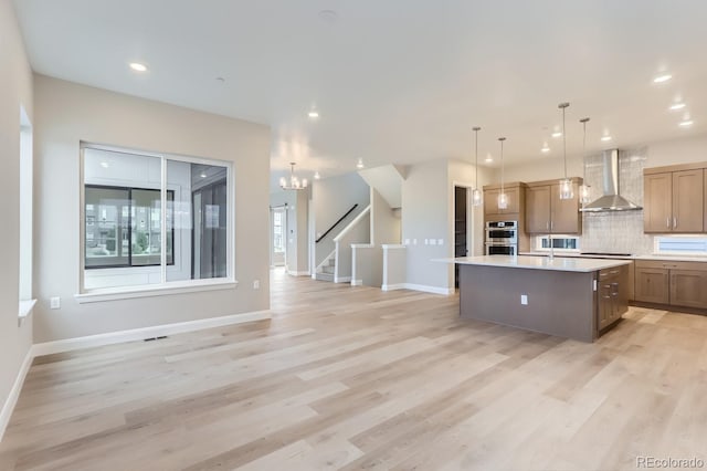 kitchen featuring backsplash, a center island with sink, black electric cooktop, decorative light fixtures, and wall chimney exhaust hood