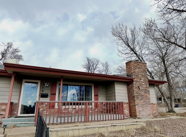 ranch-style home with a porch, a chimney, and brick siding