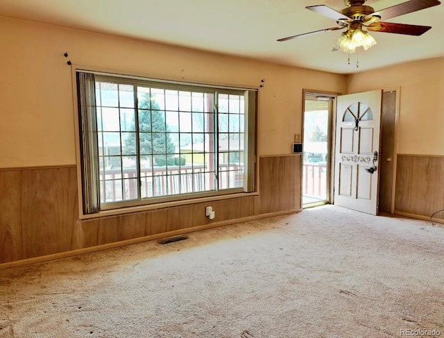 empty room featuring ceiling fan, wood walls, wainscoting, and carpet flooring