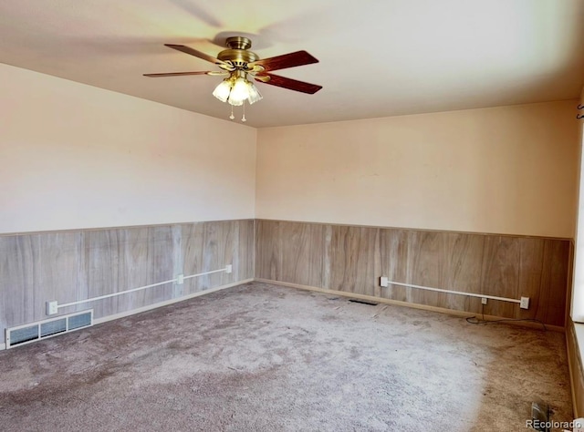 unfurnished room with a wainscoted wall, wooden walls, visible vents, and carpet flooring