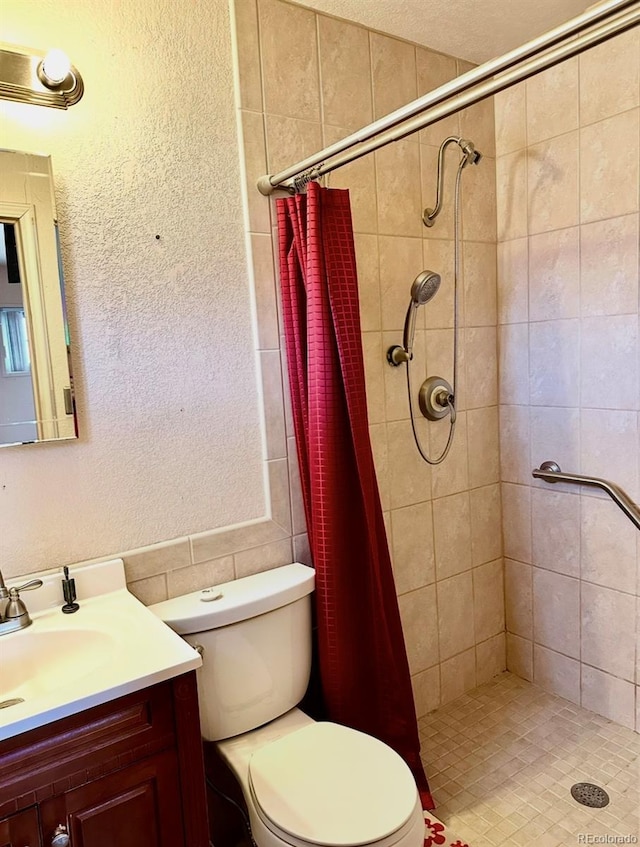 bathroom featuring a stall shower, a textured wall, vanity, and toilet