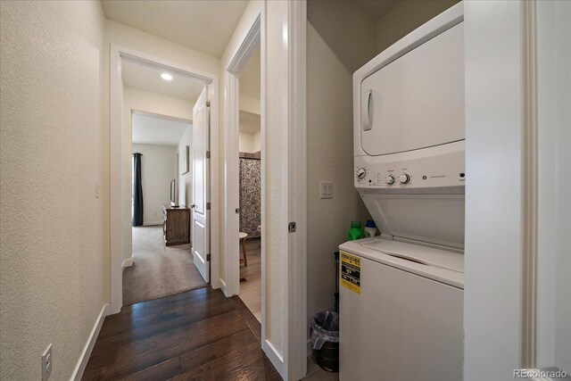 laundry area with a textured wall, laundry area, stacked washer / dryer, baseboards, and dark wood finished floors