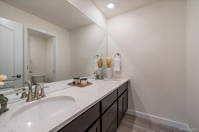 bathroom with double vanity, a sink, toilet, and baseboards