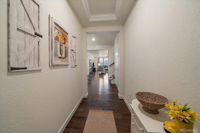 corridor with a tray ceiling, a textured wall, dark wood-style flooring, and baseboards