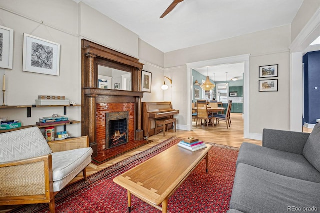 living room featuring ceiling fan, a fireplace, baseboards, and wood finished floors