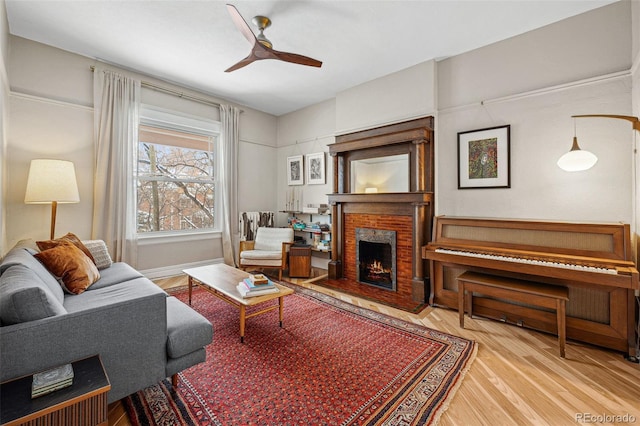 living room featuring a brick fireplace, wood finished floors, a ceiling fan, and baseboards