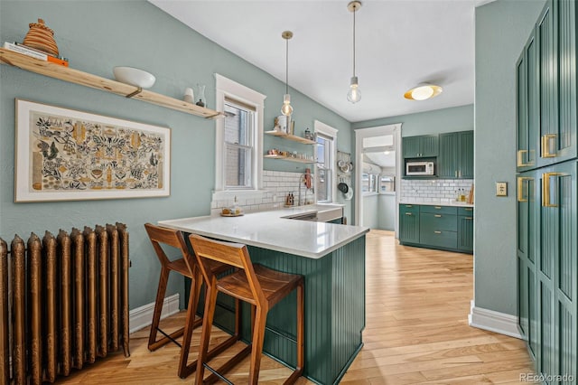 kitchen featuring radiator, white microwave, a kitchen breakfast bar, a peninsula, and green cabinetry