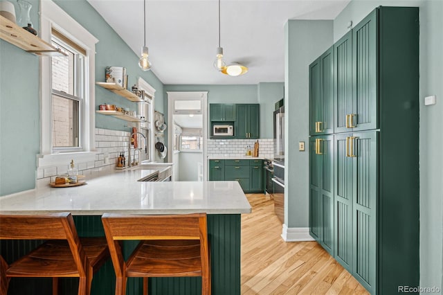 kitchen featuring white microwave, light stone counters, a peninsula, light wood-type flooring, and green cabinetry