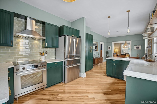 kitchen with green cabinets, appliances with stainless steel finishes, light wood-type flooring, and wall chimney range hood