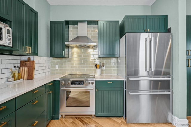 kitchen with wall chimney exhaust hood, appliances with stainless steel finishes, light wood-style flooring, and green cabinetry