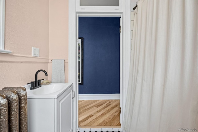 bathroom featuring a textured wall, vanity, baseboards, and wood finished floors