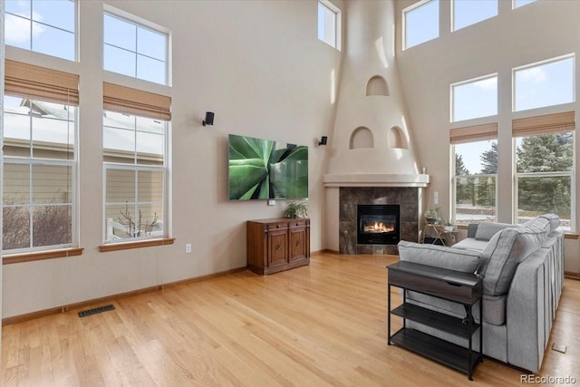 living room with a wealth of natural light, a high ceiling, light hardwood / wood-style floors, and a tiled fireplace