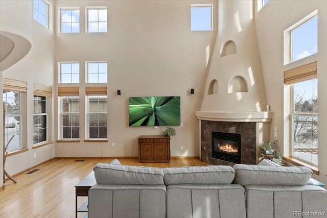 living room with a tile fireplace, plenty of natural light, light hardwood / wood-style flooring, and a high ceiling