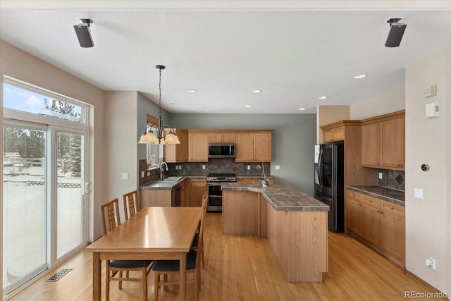 kitchen featuring appliances with stainless steel finishes, tasteful backsplash, hanging light fixtures, sink, and a kitchen island