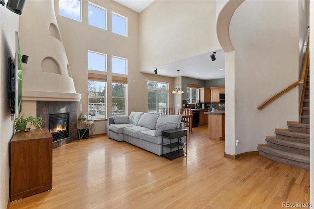 living room featuring stairway, baseboards, a high ceiling, a tile fireplace, and light wood-type flooring