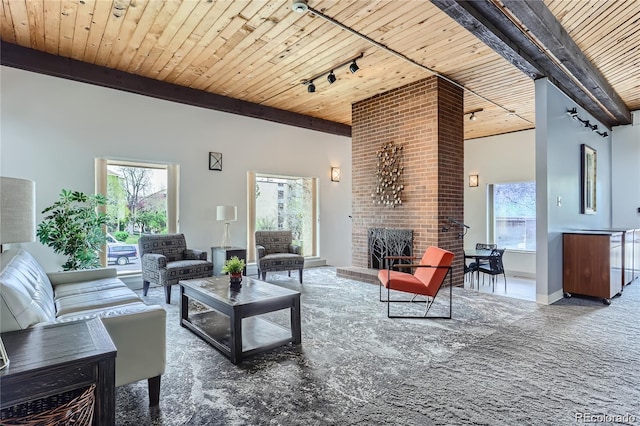 living room featuring a brick fireplace, beamed ceiling, rail lighting, and wood ceiling