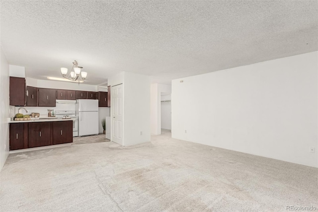 unfurnished living room featuring light colored carpet, a textured ceiling, and a notable chandelier