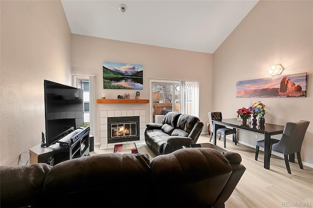 living room with a tile fireplace, vaulted ceiling, and light hardwood / wood-style flooring