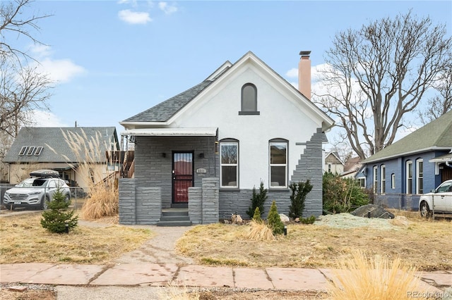 view of front facade with stone siding, a chimney, and stucco siding