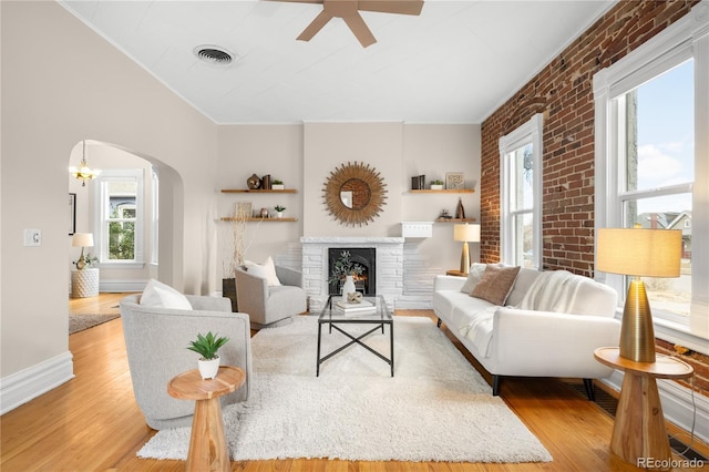 living area with light wood finished floors, visible vents, arched walkways, baseboards, and a lit fireplace