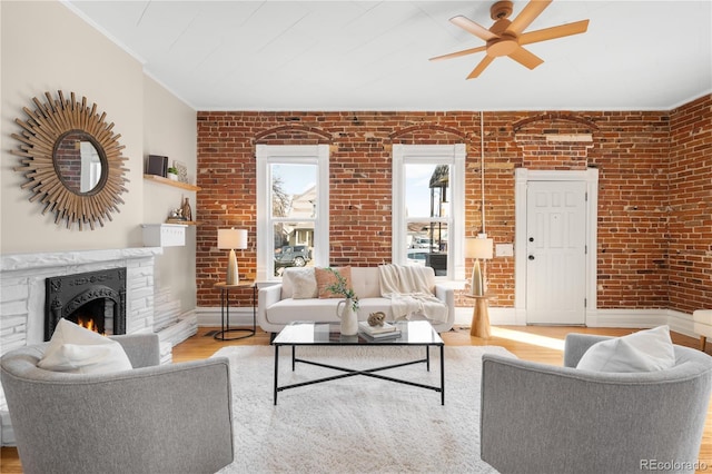 living area featuring baseboards, a fireplace, light wood-style flooring, and brick wall