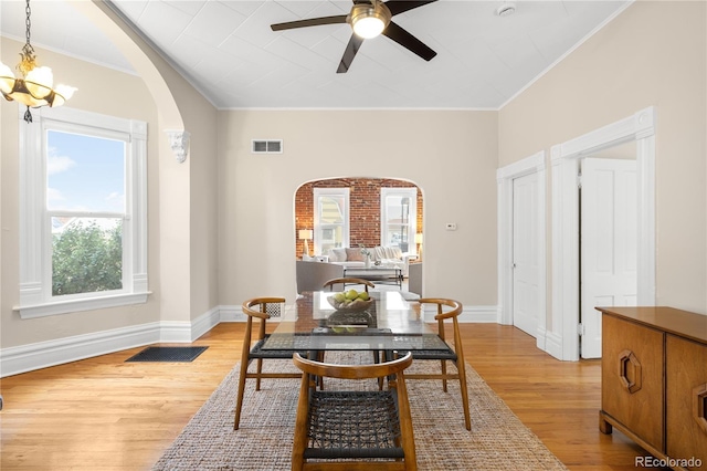 dining area with arched walkways, visible vents, baseboards, light wood finished floors, and crown molding