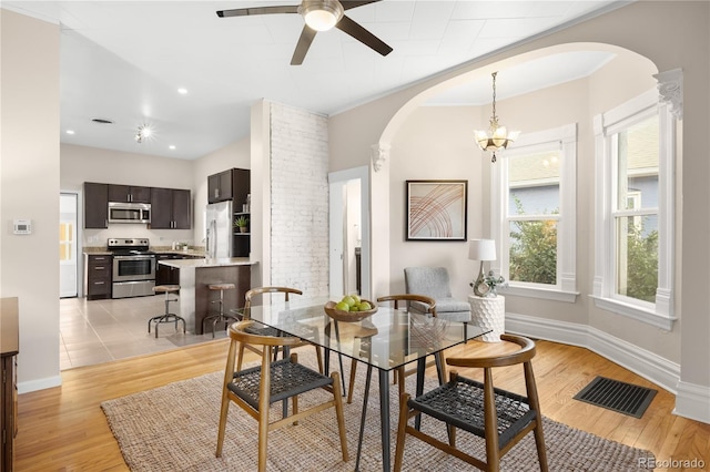 dining space featuring arched walkways, light wood finished floors, visible vents, baseboards, and ceiling fan with notable chandelier