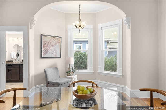 sitting room featuring light wood-style floors, arched walkways, crown molding, and baseboards