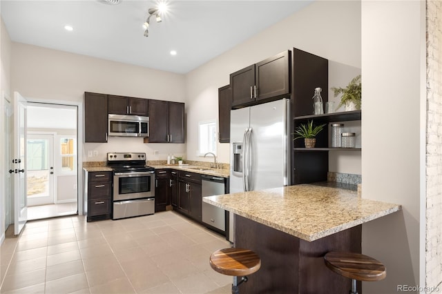 kitchen with open shelves, appliances with stainless steel finishes, a sink, a peninsula, and a kitchen bar