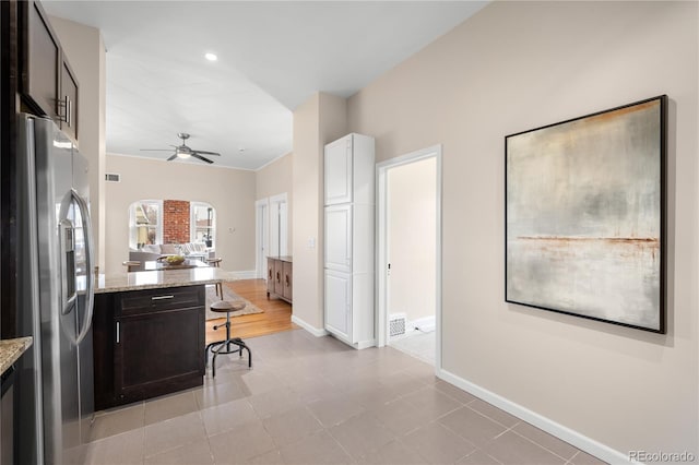 kitchen with arched walkways, a breakfast bar area, white cabinetry, light stone countertops, and stainless steel fridge with ice dispenser