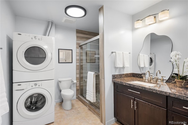 bathroom featuring tile patterned flooring, toilet, stacked washer and dryer, vanity, and a stall shower