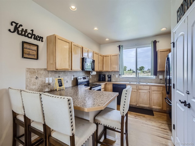 kitchen featuring backsplash, black appliances, a kitchen bar, light brown cabinetry, and kitchen peninsula