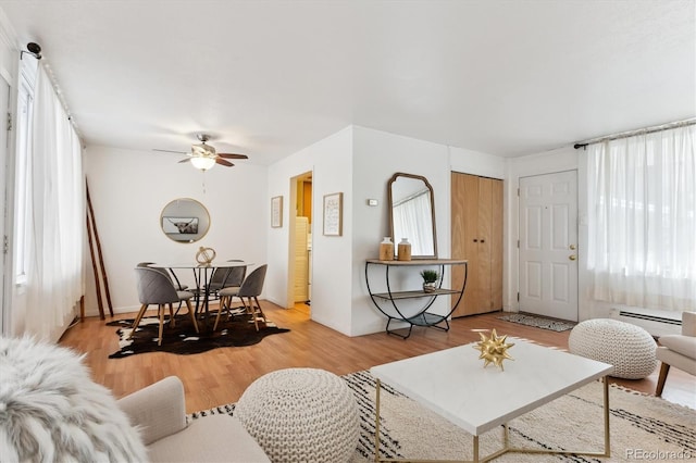 living room with a baseboard heating unit, light hardwood / wood-style floors, and ceiling fan