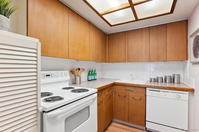 kitchen with light countertops, decorative backsplash, brown cabinetry, a sink, and white appliances