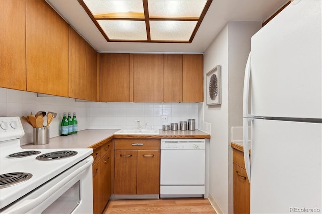 kitchen featuring light wood finished floors, tasteful backsplash, light countertops, a sink, and white appliances